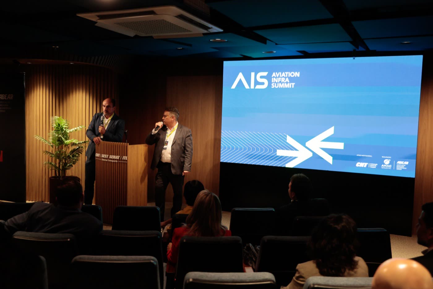 Palestrantes no palco da 1ª edição do AIS, com a marca do evento ao fundo